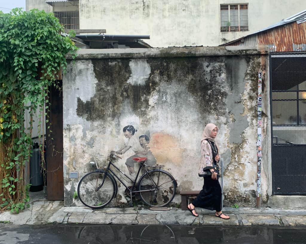 Woman walks by "Kids on Bicycle" street art located along Armenian Street